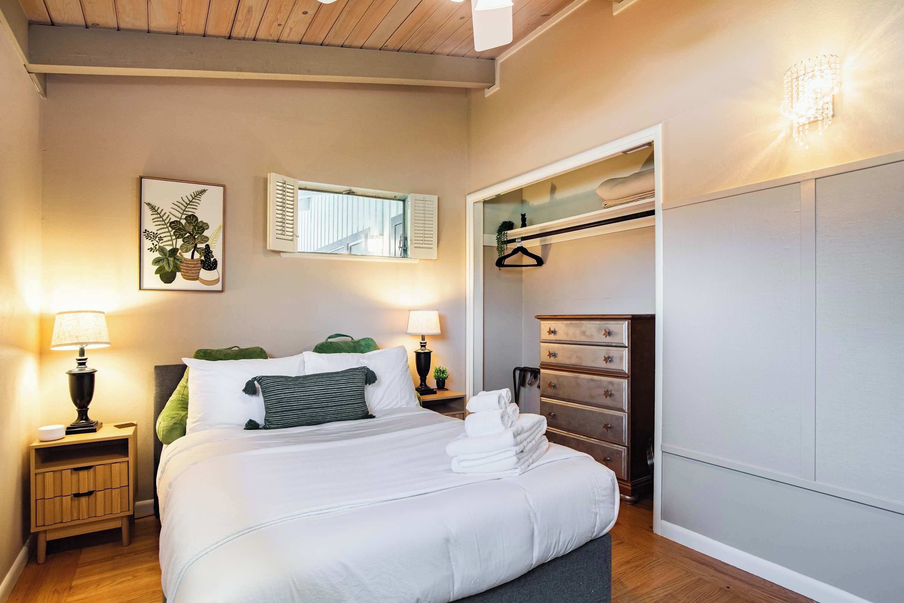 A neatly arranged bedroom with a bed, bedside lamps, a hanging plant, and a wardrobe.