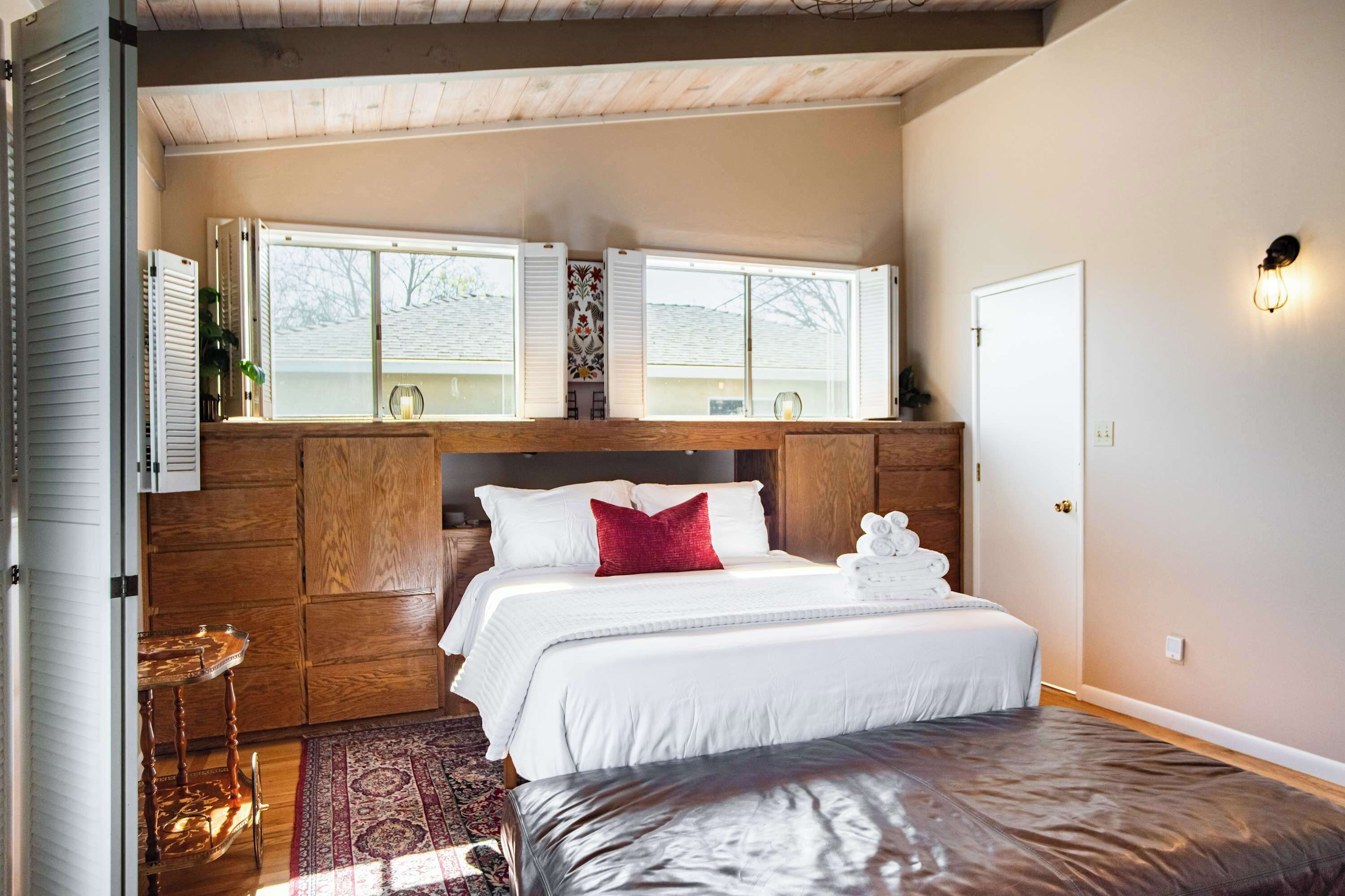 Une chambre à coucher avec un lit, une tête de lit en bois, des fenêtres et une porte.