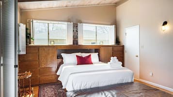 Une chambre à coucher avec un lit, une tête de lit en bois, des fenêtres et une porte.