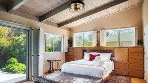 A bedroom with a large bed, a wooden headboard, a window with blinds, a wooden ceiling, and a view of greenery outside. - Spacious 4BR Backyard Oasis with BBQ Near UC Davis (Davis)