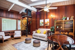 Un vaste salon doté d’un haut plafond, de murs en bois, d’un escalier en colimaçon, d’un canapé avec des coussins, d’une table à manger avec des chaises et d’une bibliothèque.