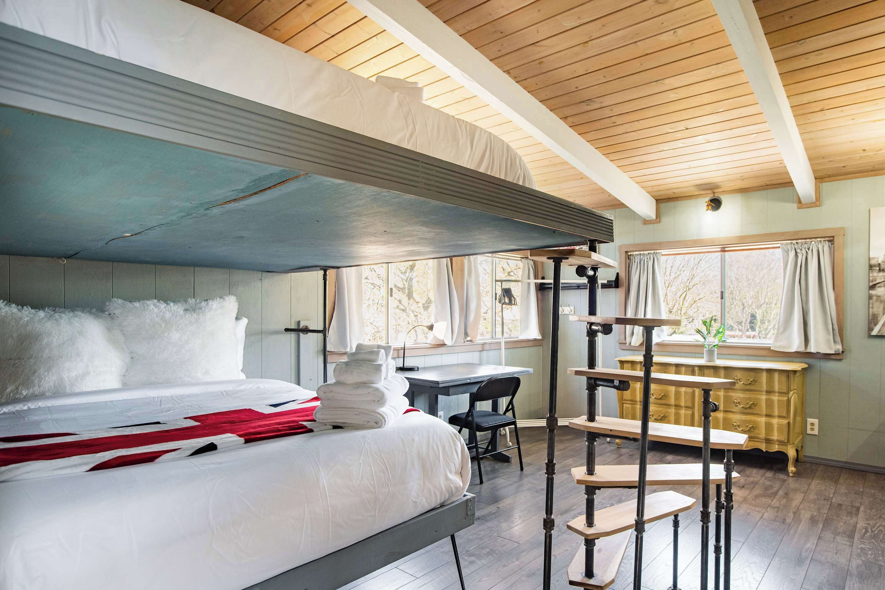 Ein Schlafzimmer mit Etagenbett, Schreibtisch, Stuhl und einem Fenster mit Vorhängen.