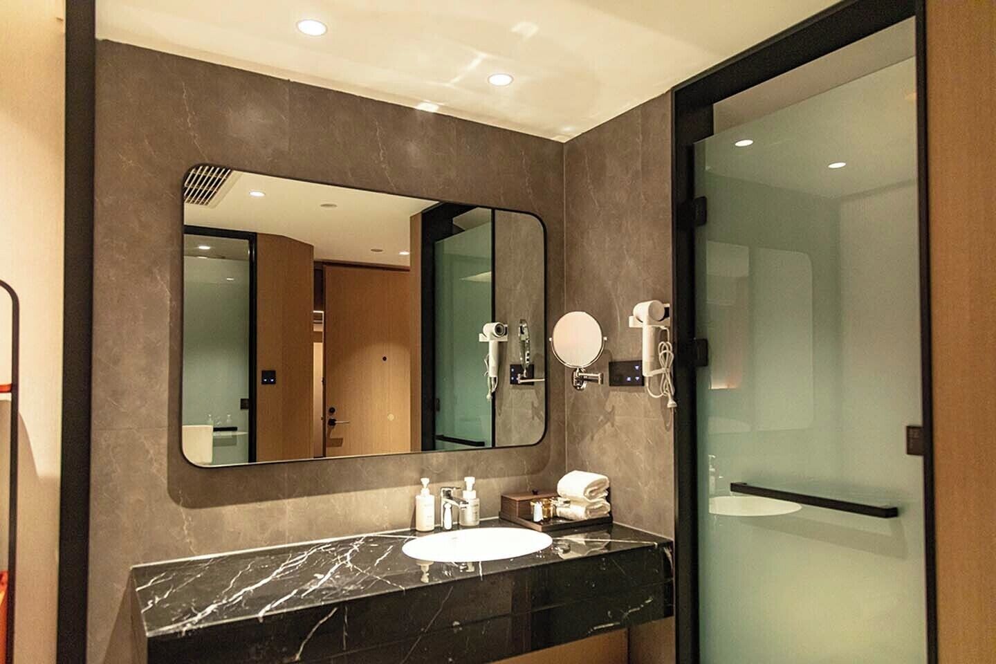 A modern bathroom with a marble sink, a large mirror, and a glass shower enclosure.