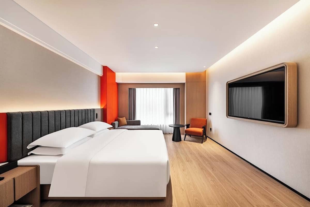 A hotel room with a bed, a TV, a chair, and a small table.