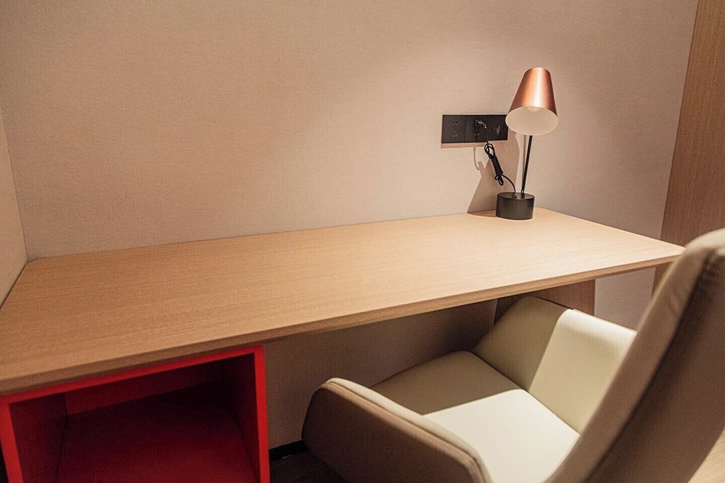 A corner desk with a chair, a lamp, and a red storage box.