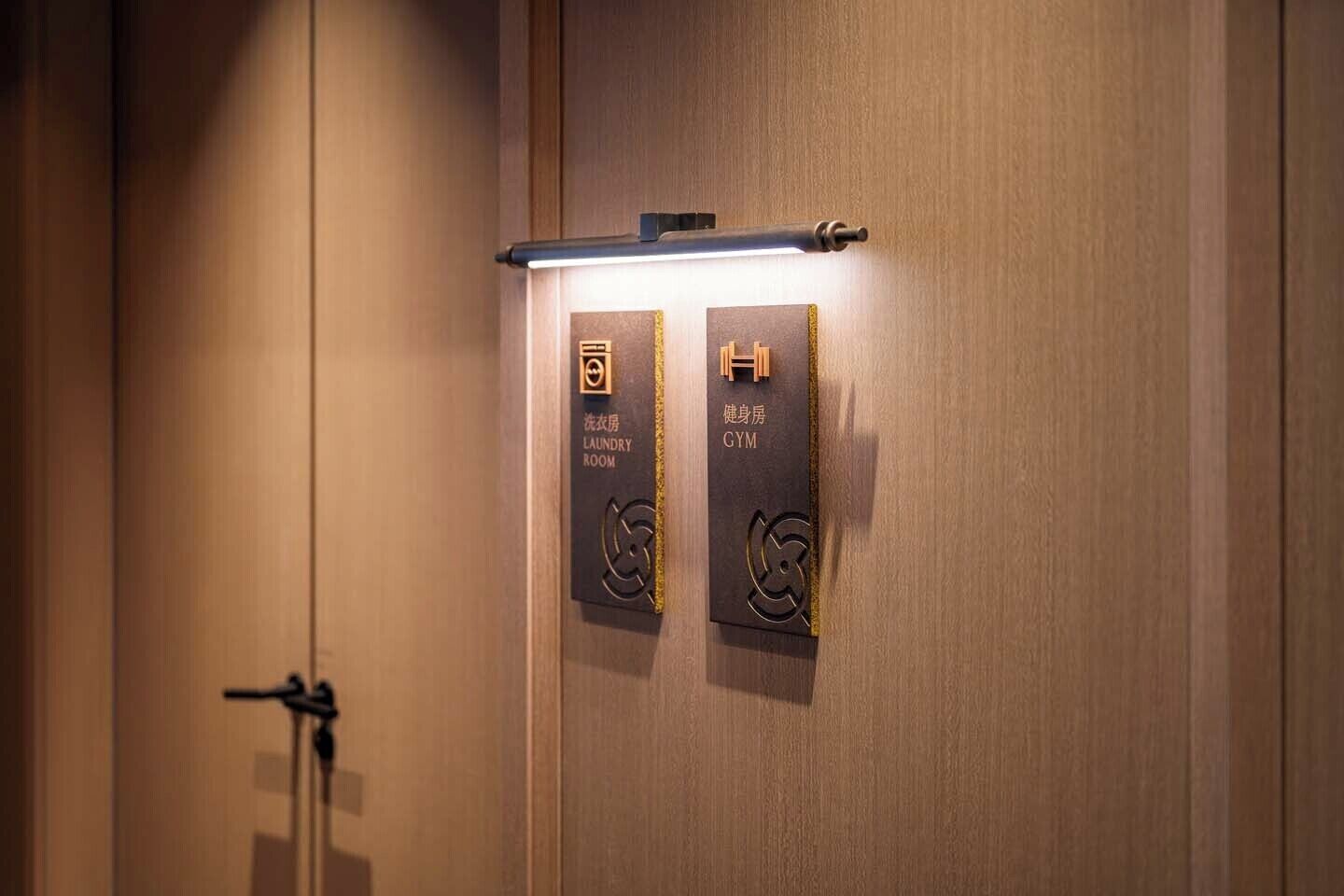 A hotel room with a wooden door, a towel rack, and two signs indicating a laundry room and a gym.