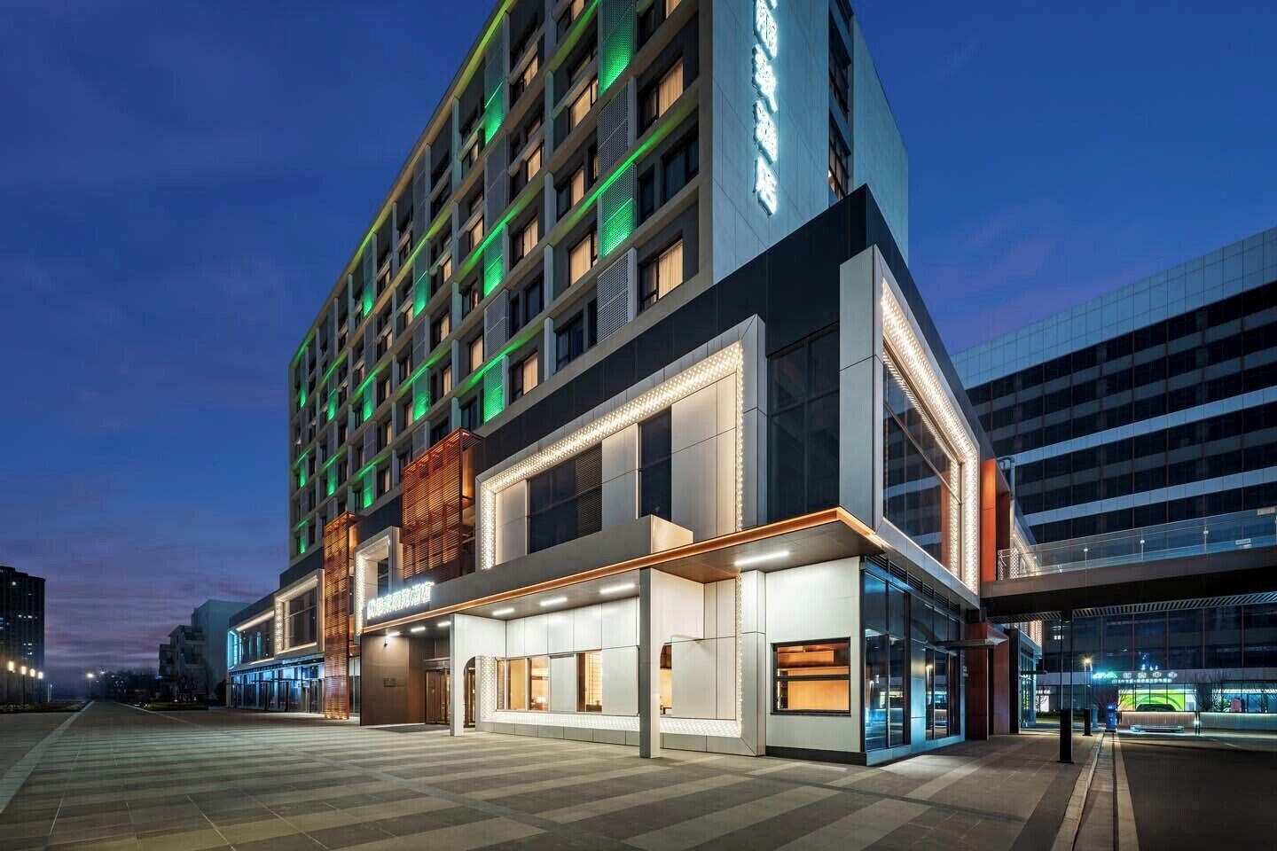 Un hotel moderno con varios pisos, ventanas amplias y una zona de entrada bien iluminada.