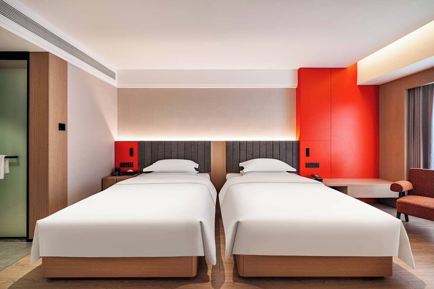 A hotel room with two beds, a desk, a chair, and a red accent wall.