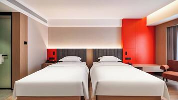 A hotel room with two beds, a desk, a chair, and a red accent wall.