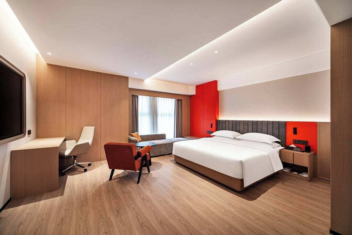 A modern hotel room with a large bed, a desk, a chair, and a sofa.