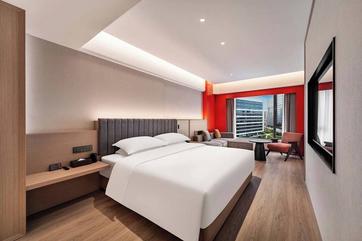 A modern hotel room with a large bed, a desk, a chair, and a view of the cityscape.