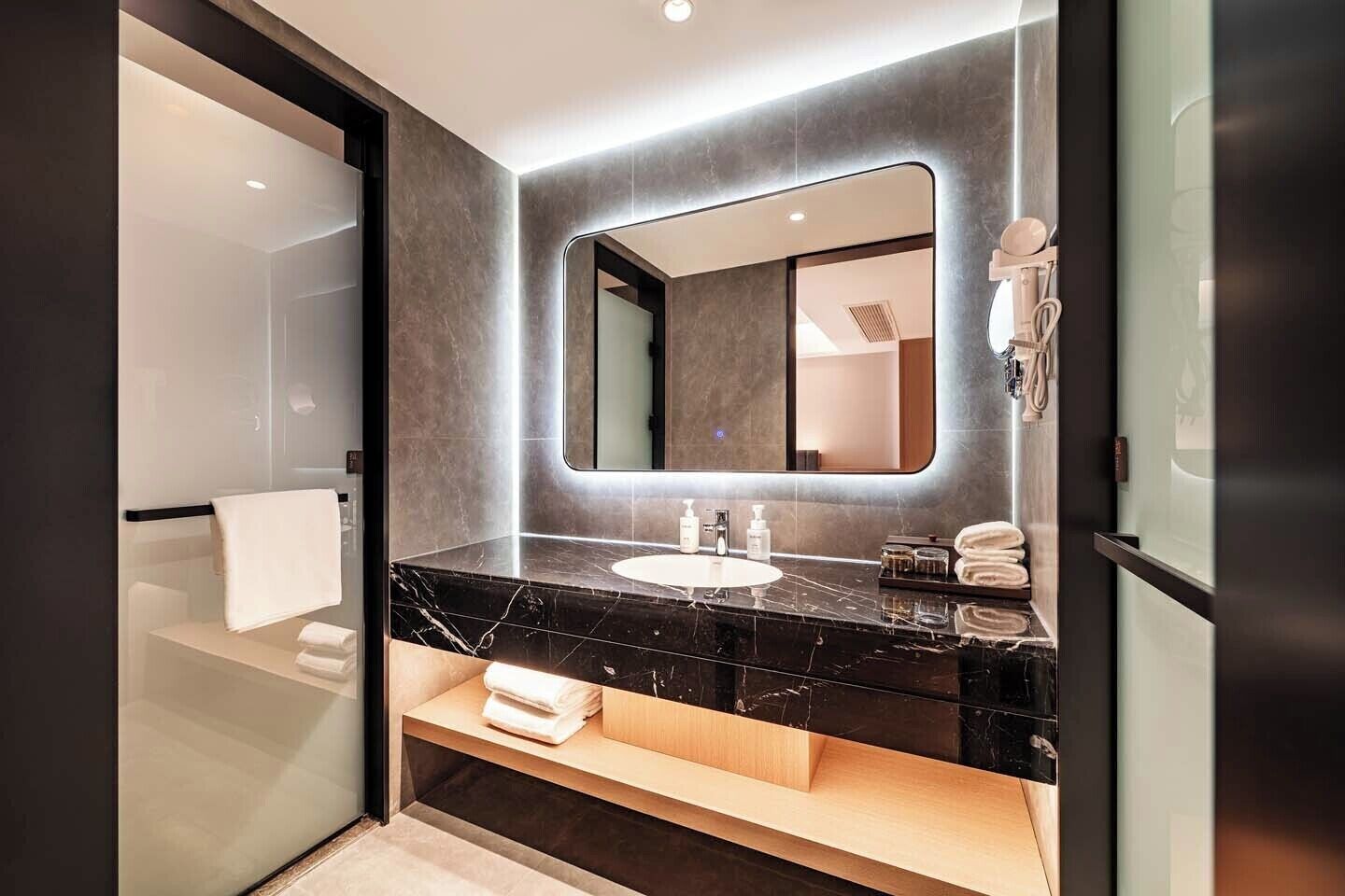 Un baño moderno con lavamanos de mármol negro, un espejo grande y un perchero para toallas.
