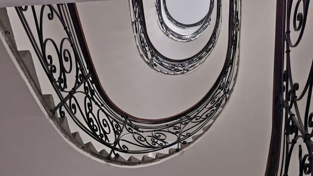 Eine Wendeltreppe mit aufwendiger Metallgeländerung und einem Fenster mit Buntglas.