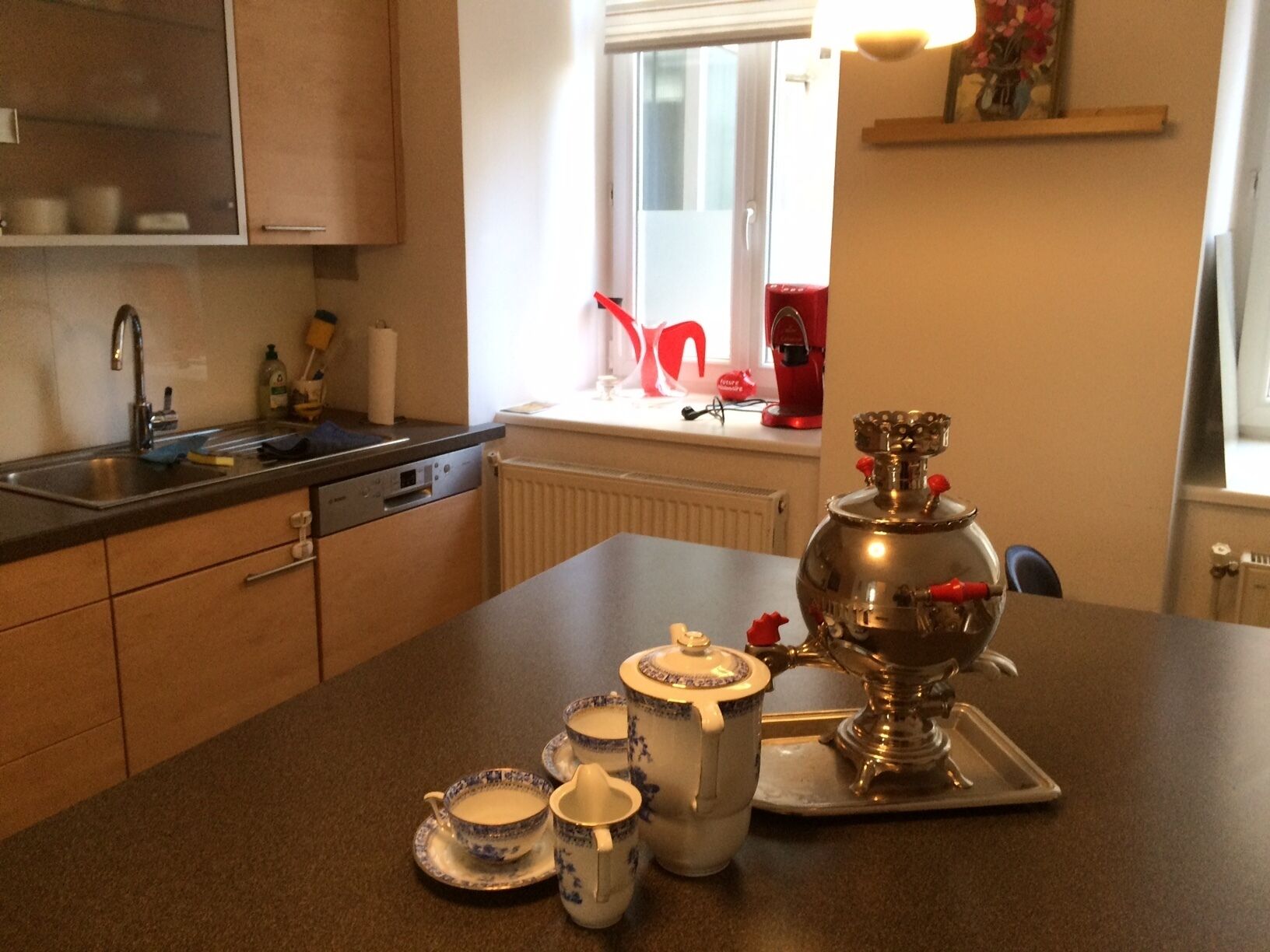 A kitchen with a sink, cabinets, a radiator, a window with a view, and a traditional stove.