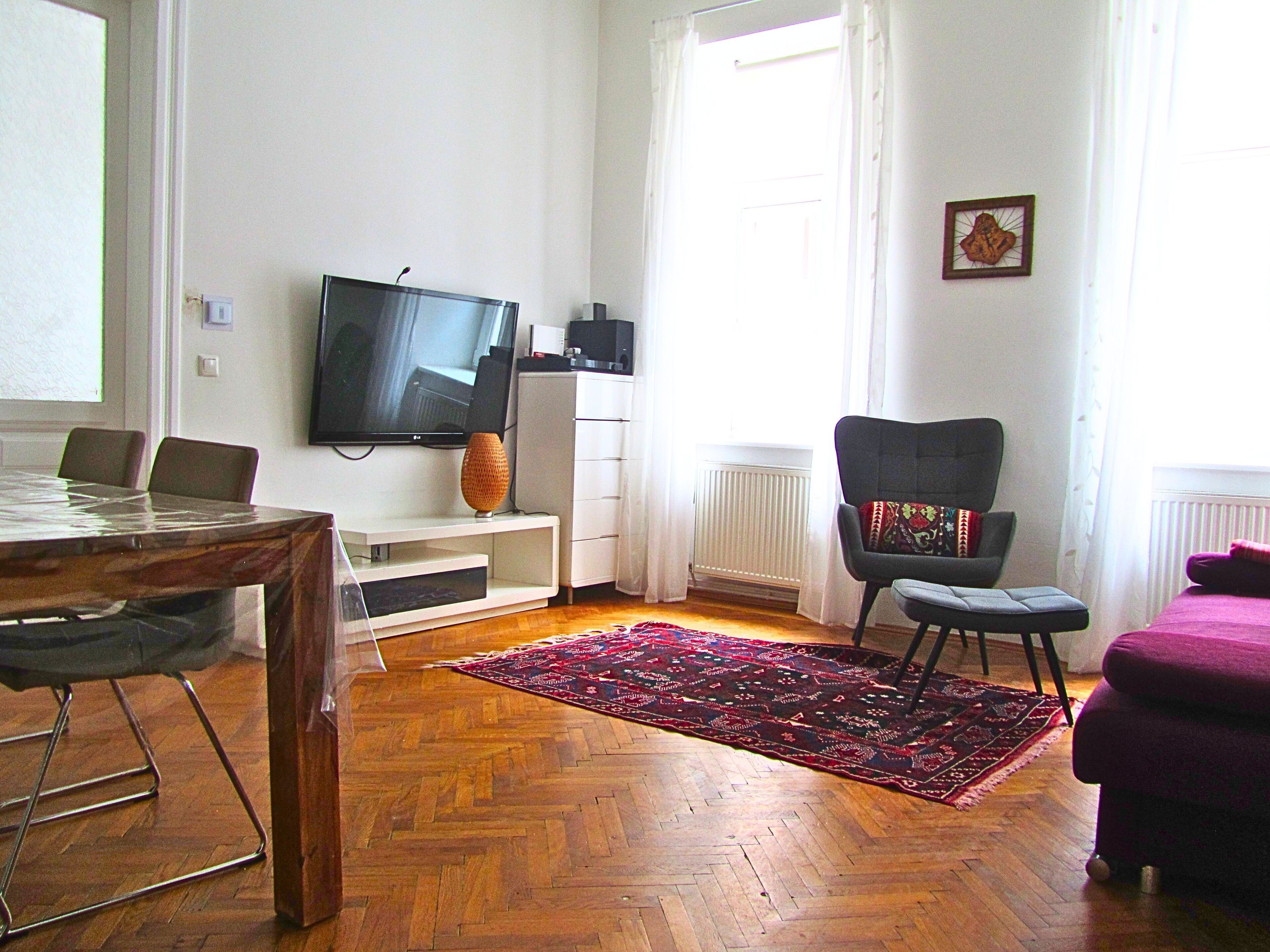 Un salon avec un téléviseur, un fauteuil, une table et un tapis à motifs.