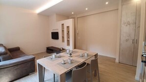 Ein modernes Wohnzimmer mit einer Couch, einem Esstisch mit Stühlen, einem Flachbildfernseher und einem Kleiderschrank.