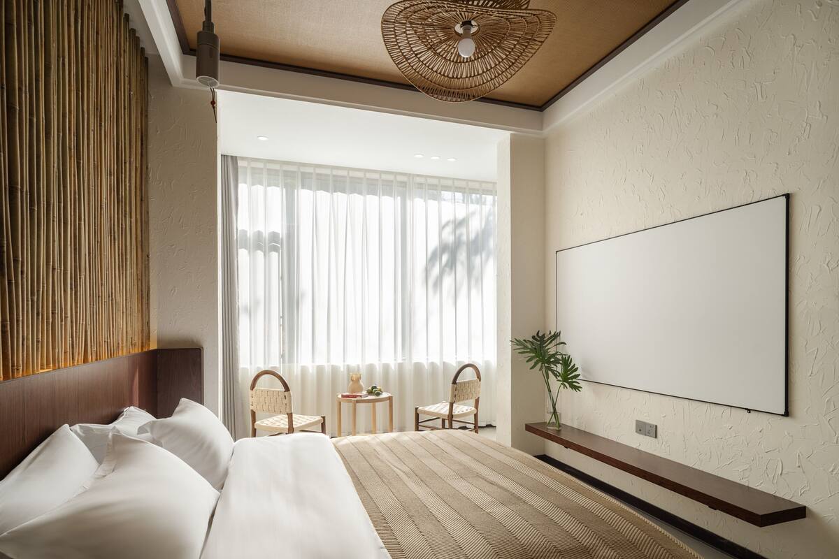 Ein modernes Hotelzimmer mit einem großen Bett, einem wandmontierten Fernseher und Blick ins Freie durch transparente Vorhänge.