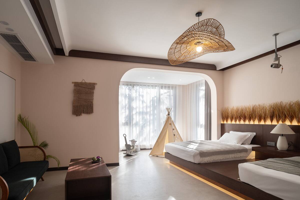 Ein modernes Hotelzimmer mit einem Bett, einem Sofa, einem Couchtisch, einer Hängeleuchte und Blick ins Freie.