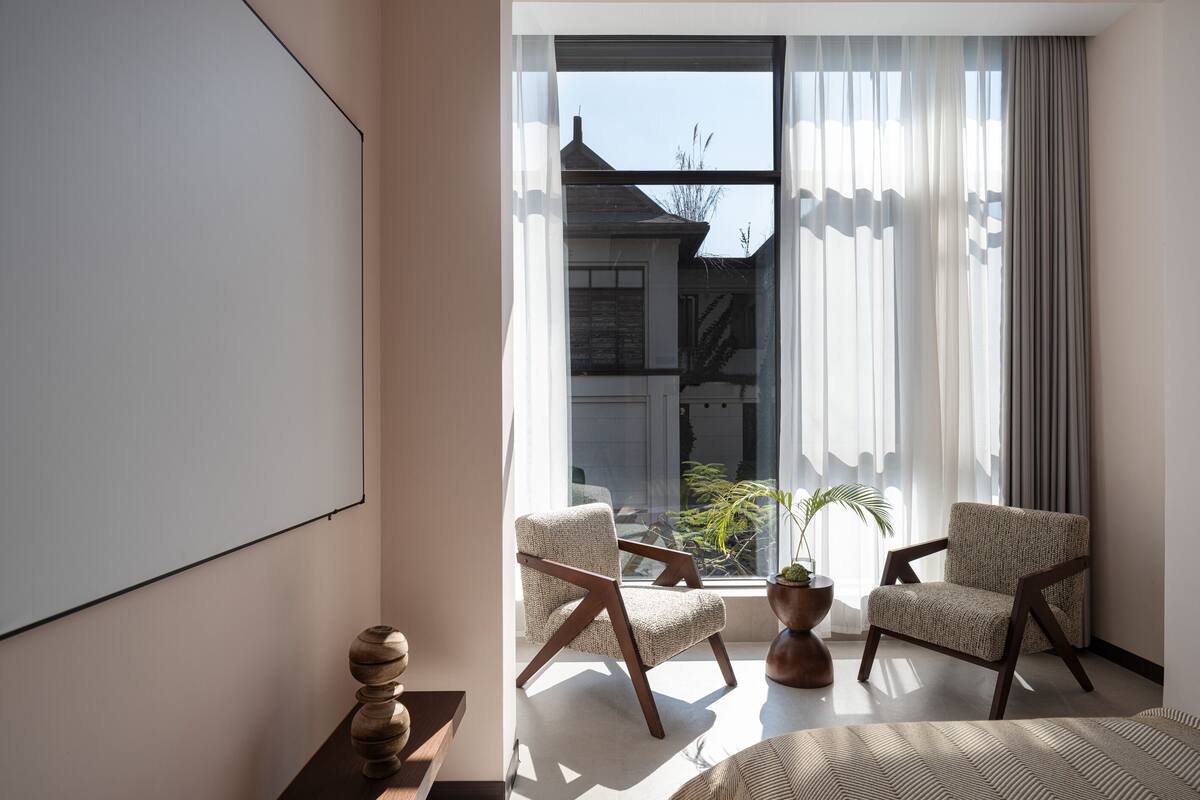 Ein modernes Zimmer mit großem Fenster, zwei Stühlen, einem kleinen Tisch und einer dekorativen Vase.