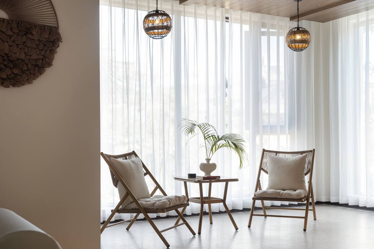 Ein Zimmer mit zwei Korbstühlen, einem kleinen Tisch mit einer Pflanze und zwei Hängeleuchten.