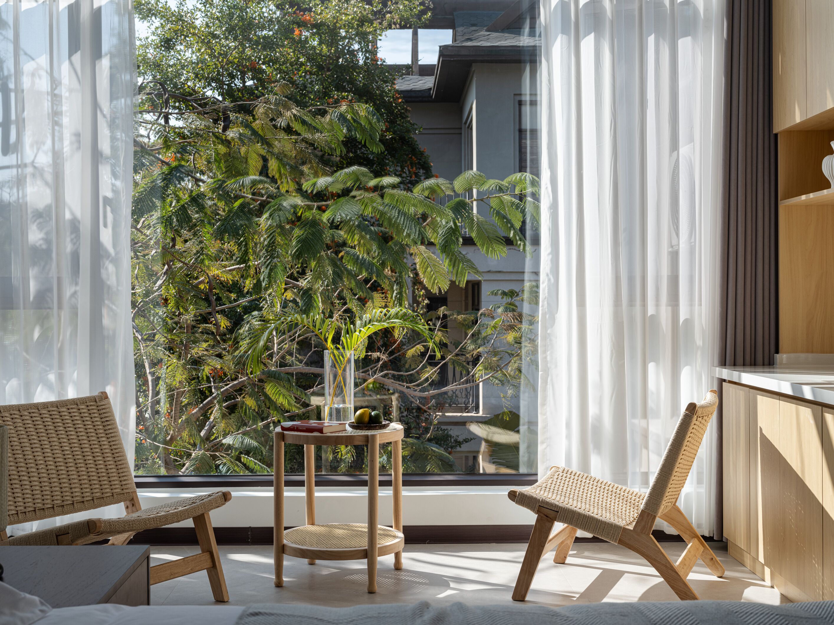 A balcony with wicker chairs, a small table, and a view of a lush green tree.