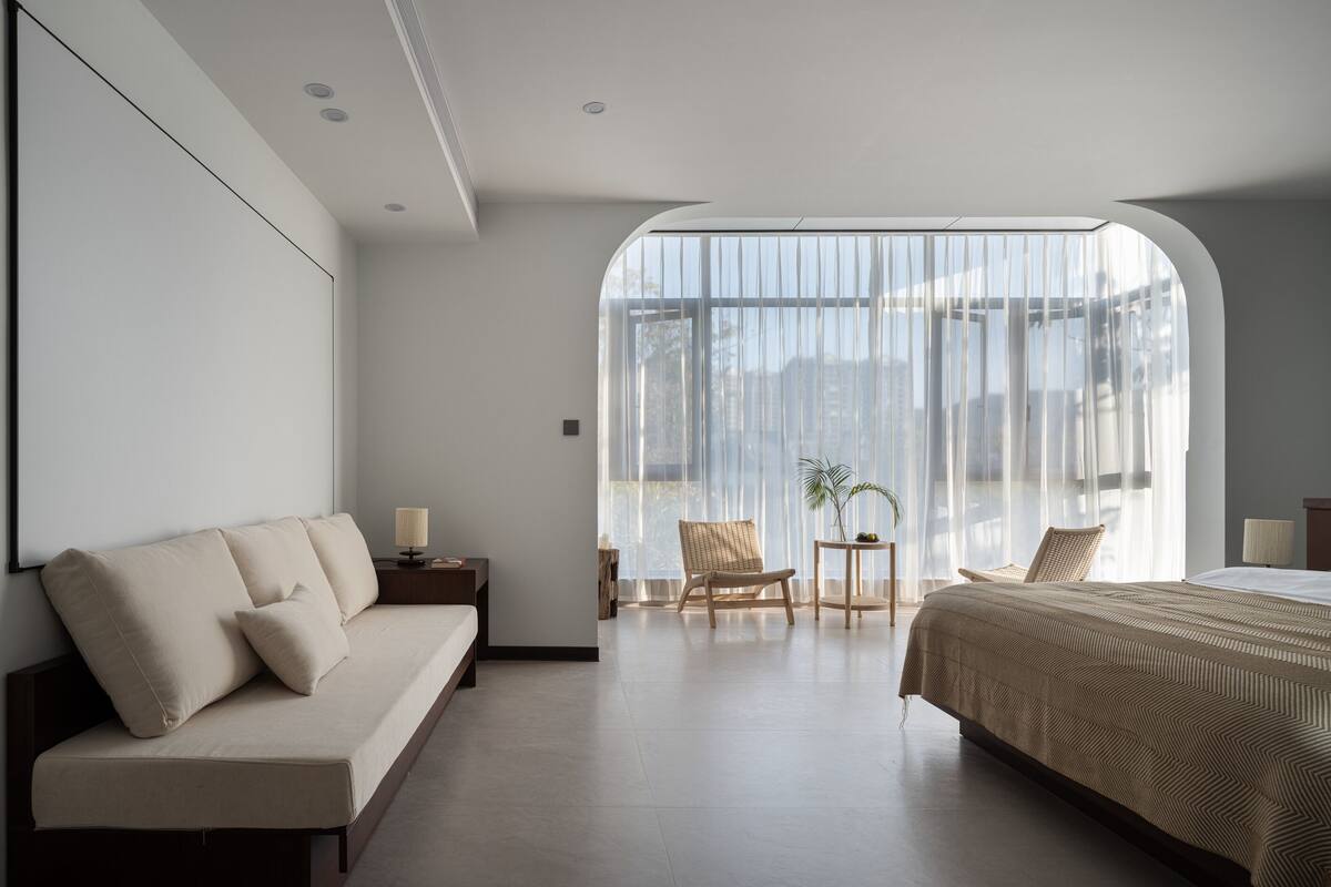 Ein modernes Hotelzimmer mit einem großen Bett, einem Sofa, einem kleinen Tisch mit Lampe und einem Sessel.