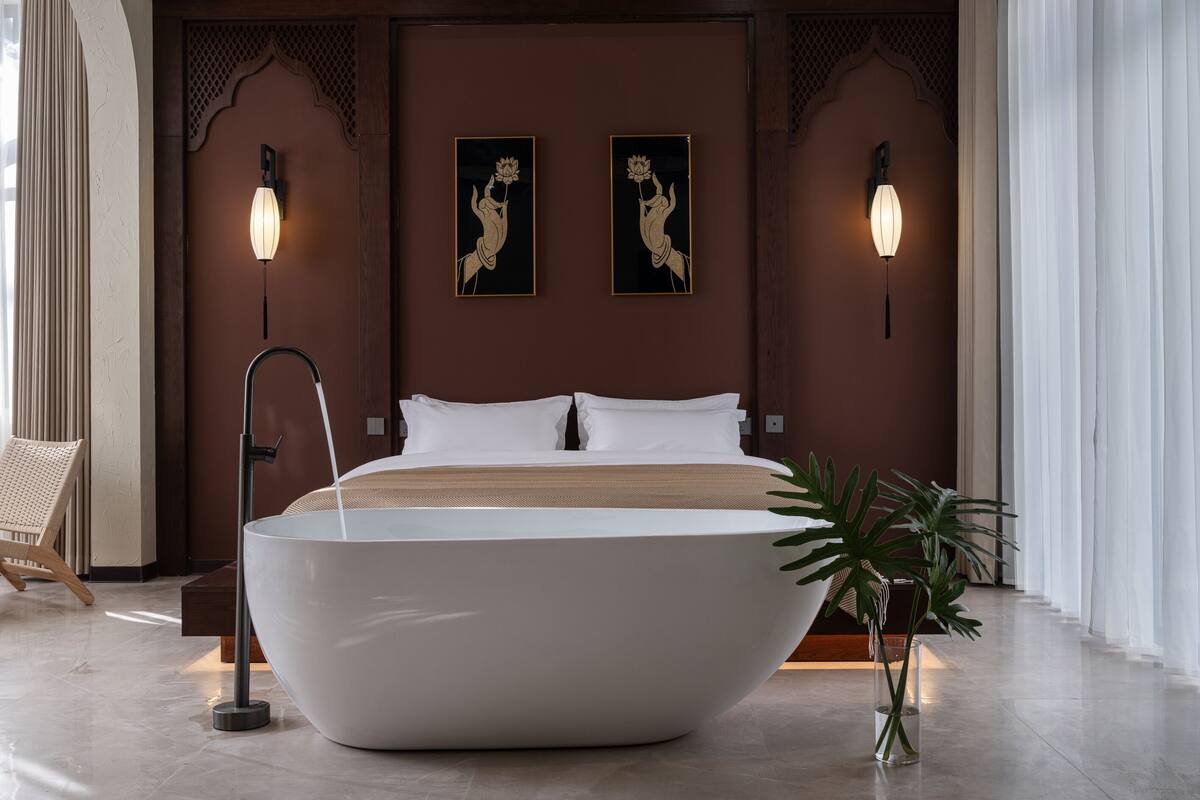 Ein modernes Hotelzimmer mit einer großen Badewanne, einem Bett mit weißen Leinen, zwei an der Wand befestigten Kunstwerken und einem Topf mit einer Pflanze.
