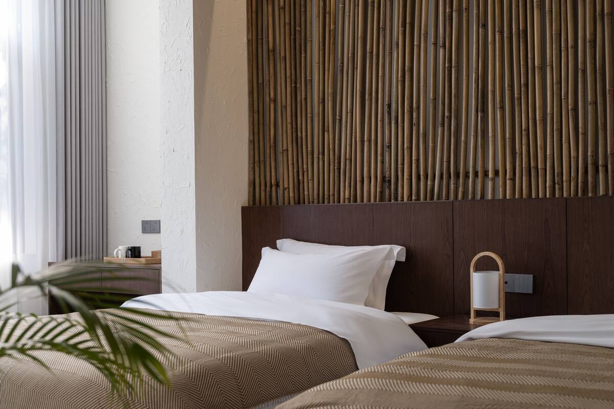 Ein Hotelzimmer mit Bett, Nachttisch, Lampe und einer Wand mit vertikalen Bambuslatten.