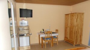 A bedroom with a bed, a desk with a chair, a television mounted on the wall, and a wardrobe.