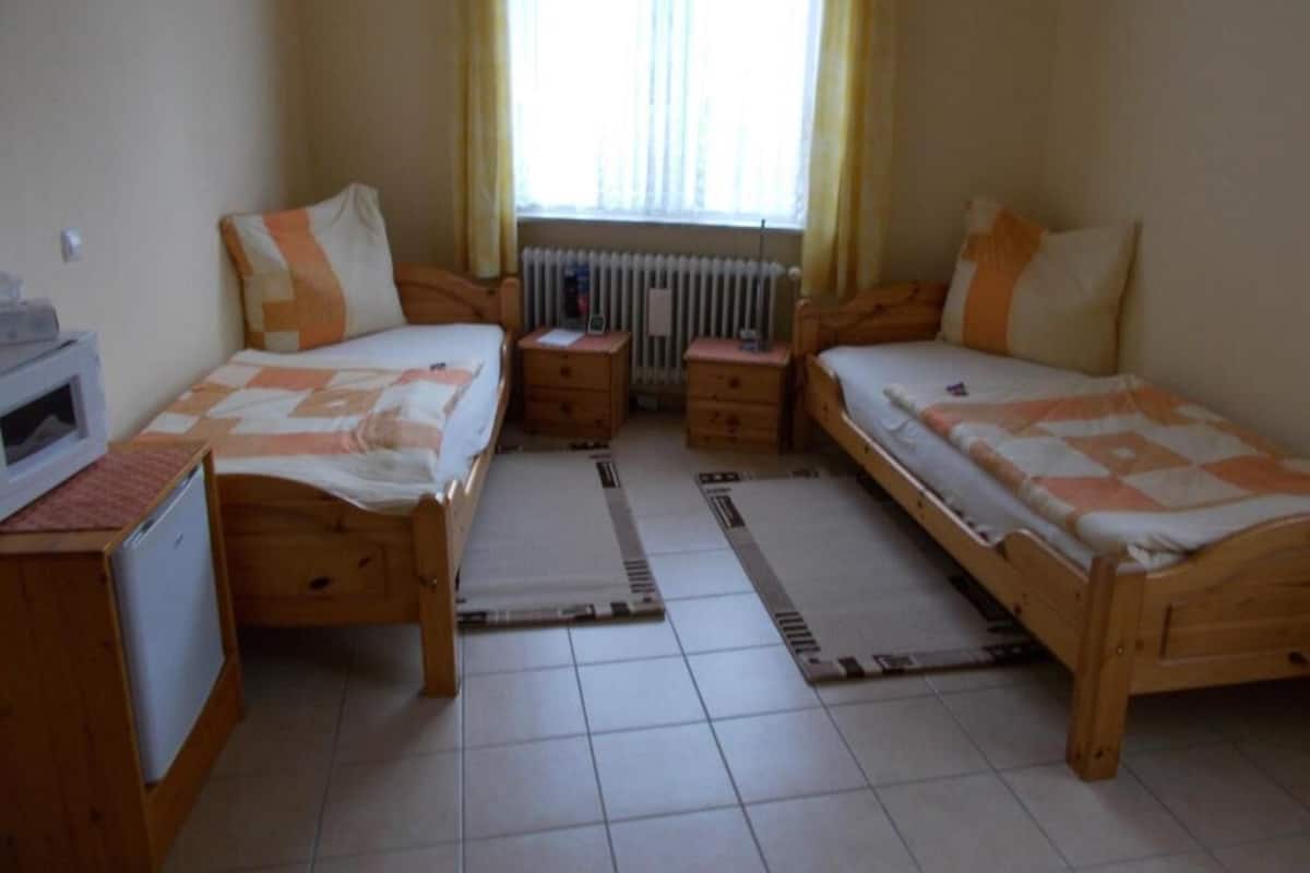 Un dormitorio con dos camas individuales, un escritorio pequeño, un radiador y una ventana con cortinas.