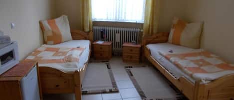 A bedroom with two single beds, a small desk, a radiator, and a window with curtains.