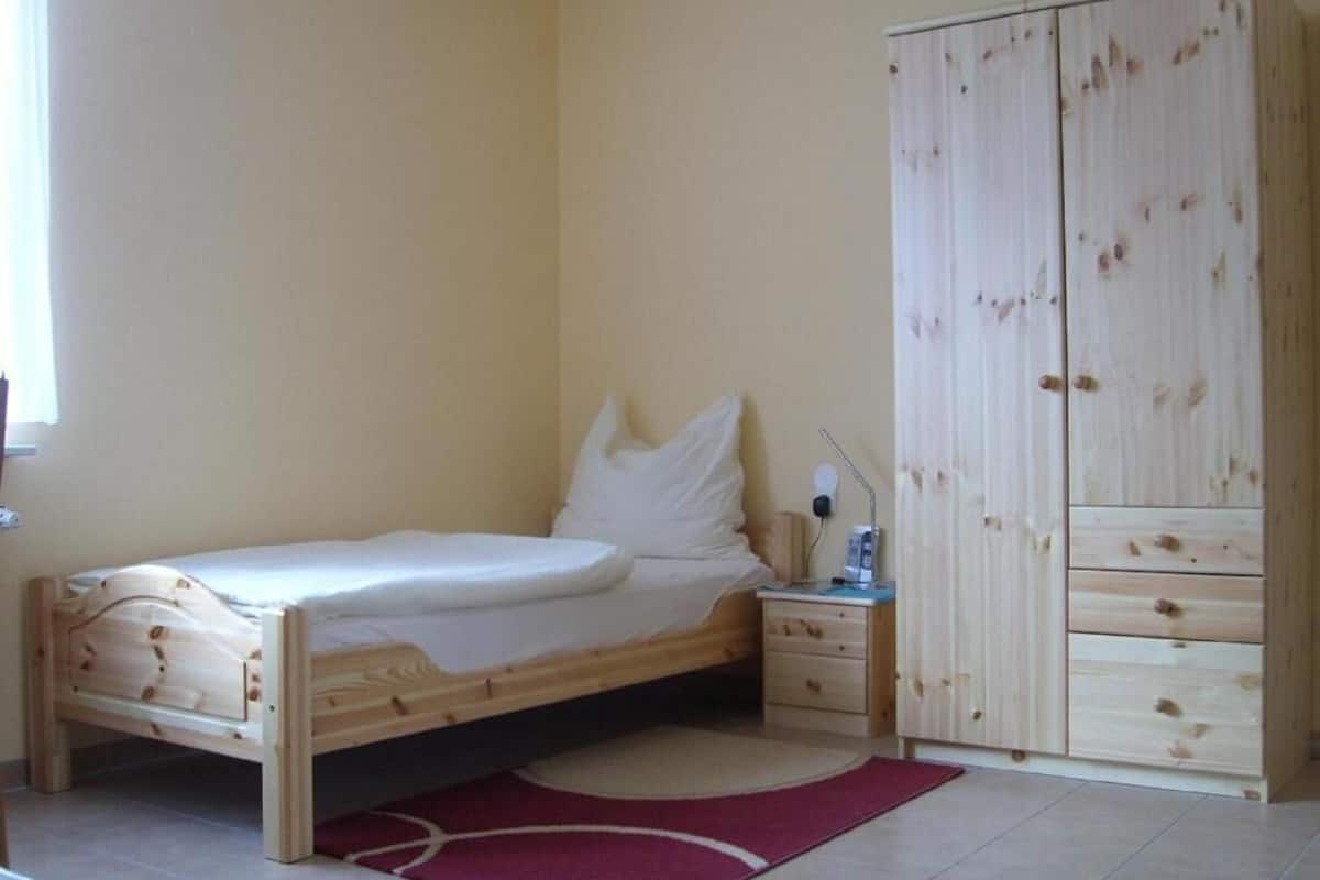 Un dormitorio con una cama de madera, una mesita de noche, un armario y una alfombra roja.