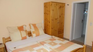 A bedroom with a bed, wooden wardrobe, and a door leading to another room.