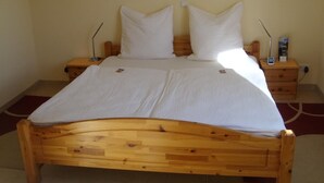 A wooden bed with white bedding, two bedside tables, and a nightstand with a lamp.