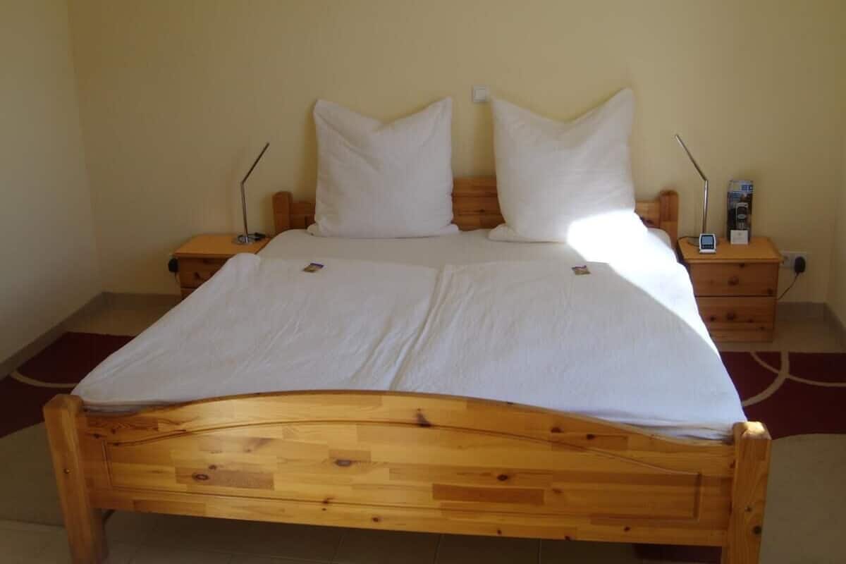 Una cama de madera con ropa blanca, dos mesitas de noche y una mesilla con una lámpara.