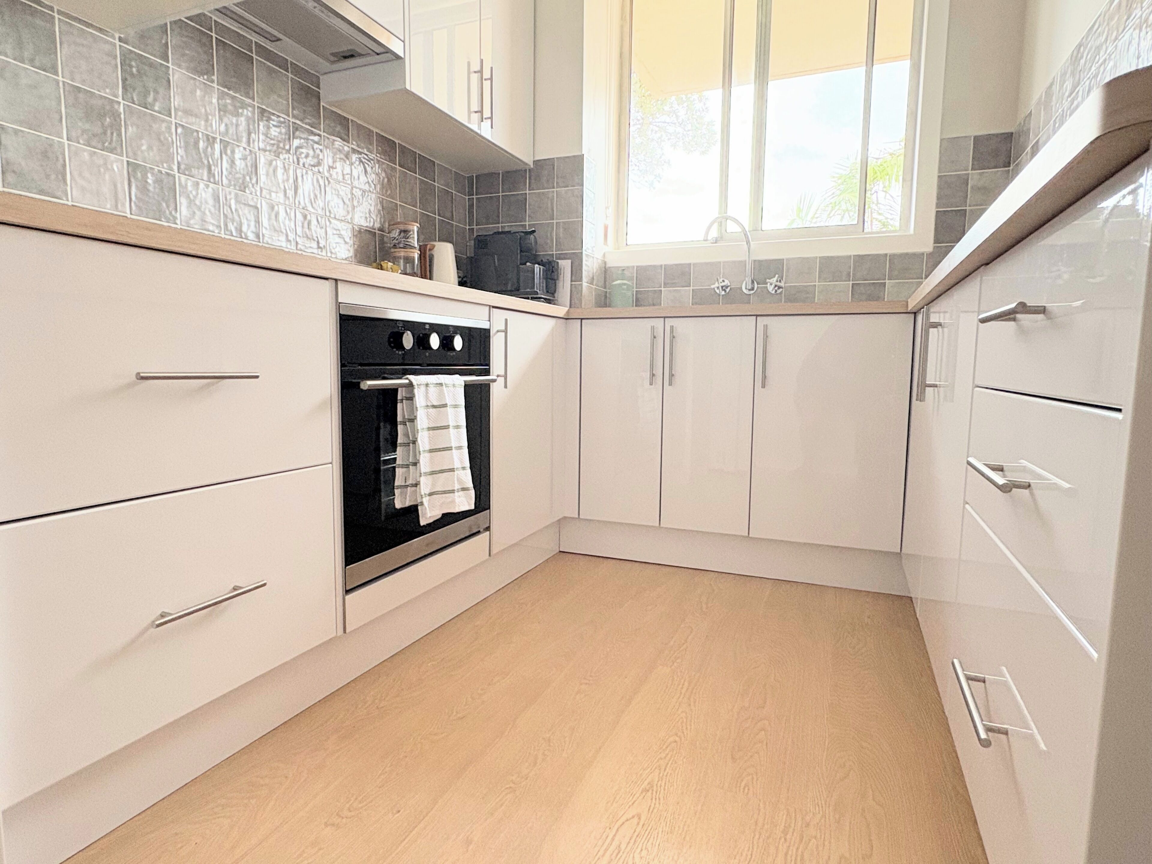 A kitchen with white cabinets, a black oven, and a window with blinds.