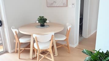 A dining area with a round table, four chairs, a potted plant, and a framed artwork on the wall.