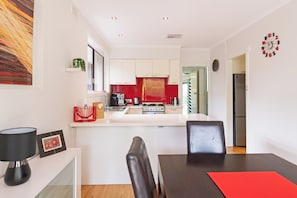 A modern kitchen with white cabinets, a red backsplash, and a central island. - Home among the Gum Trees - free wine (Tea Tree Gully)