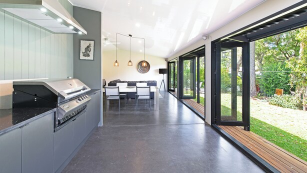A modern kitchen with a built-in grill, a dining area with a table and chairs, and large sliding glass doors leading to a garden. - Home among the Gum Trees - free wine (Tea Tree Gully)