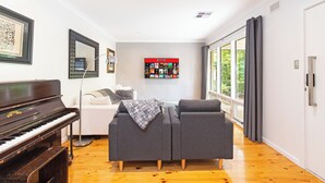 A living room with a piano, grey sofa, and a wall with Netflix posters. - Home among the Gum Trees - free wine (Tea Tree Gully)