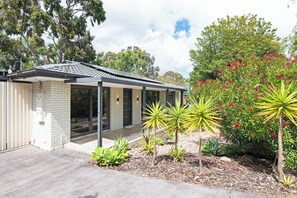A modern house with a tiled roof, a covered porch, and a garden with various plants and a tree with pink flowers.