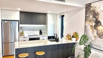 A modern kitchen with a central island, bar stools, a stainless steel refrigerator, and a large abstract painting on the wall.
