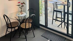 Een moderne kamer met een glazen tafel en stoelen, uitzicht op de stad door grote ramen, en een schilderij aan de muur.