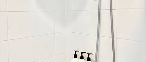 A shower with a handheld showerhead and a fixed rain showerhead, a handheld soap dispenser, and a soap dish with a bar of soap.