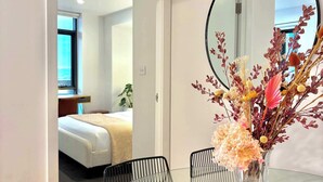 A hotel room with a bed, a bedside table, a mirror, and a glass table with chairs. - Newcastle Harbour, 2-Apartments 4-Bed 4-Bath 2-Car (Wickham)