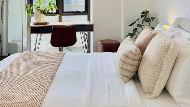 Ein Hotelzimmer mit Bett, Schreibtisch, Stuhl, Fenster und Pflanze.