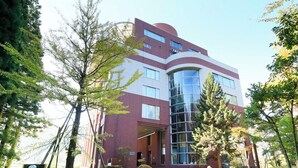 Un edificio moderno con fachada de vidrio, rodeado de árboles y un acceso pavimentado.