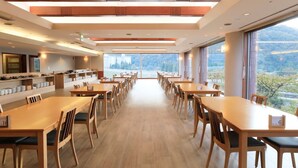A spacious dining area with long tables and chairs, large windows offering a view of the outdoors, and a modern ceiling design. - Yutorelo Echigoyuzawa  (Yuzawa)