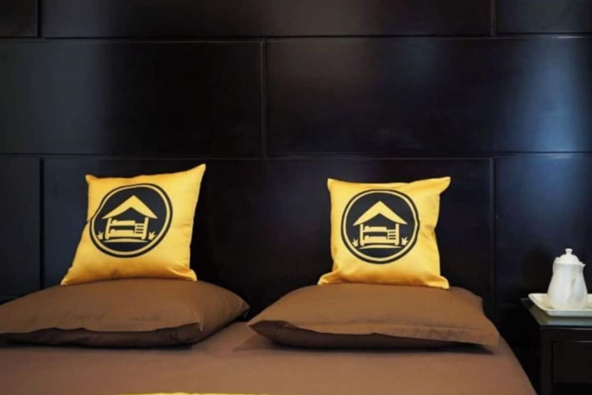 A bed with two pillows, a nightstand with a white object, and a dark wall.