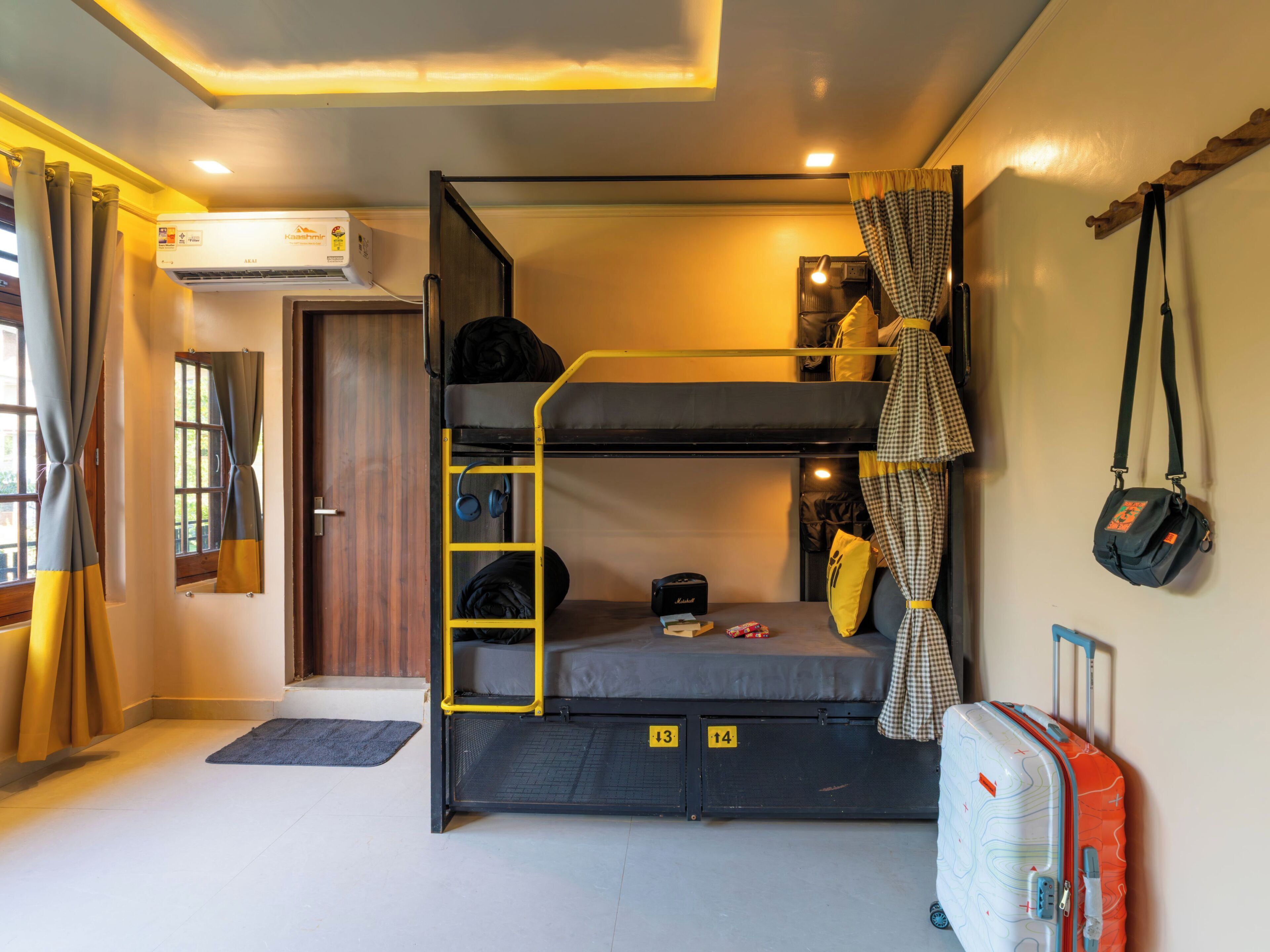 Habitación con literas, una escalera, una maleta y un bolso en el suelo.